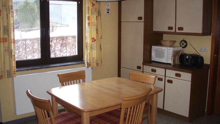 A cozy kitchen with a wooden table and chairs. In the background, a window and some kitchen cabinets are visible.