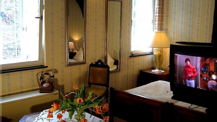 Ein gemütliches Zimmer mit einem Tisch, auf dem eine Vase mit Tulpen steht. Ein Fernseher und ein Fenster mit Tageslicht sind ebenfalls sichtbar.