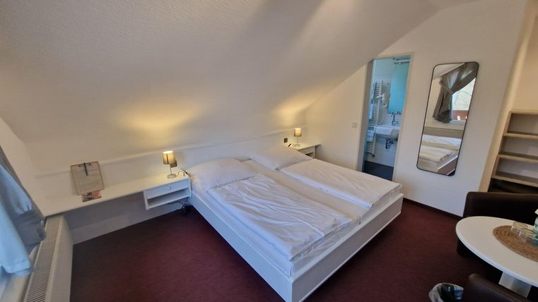 A cozy bedroom with two single beds and warm lighting. In the background, a modern bathroom area is visible.