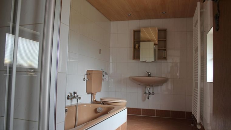 A modern bathroom with a bathtub, a sink, and a toilet. The walls are brightly tiled and there is a wooden ceiling with integrated lighting.