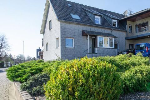 Ein modernes Haus mit grauer Fassade und einem gepflegten Garten. Vor dem Gebäude sind grüne Sträucher und ein Parkplatz mit einem blauen Auto zu sehen.