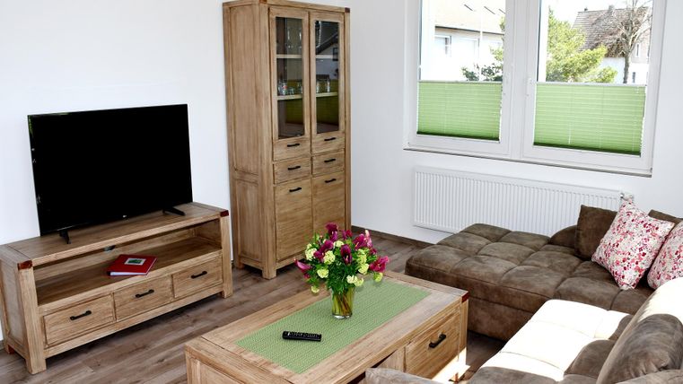 Een moderne woonkamer met een televisie, een elegante houten kast en een comfortabele bank. Op de tafel staat een vaas met kleurrijke bloemen.