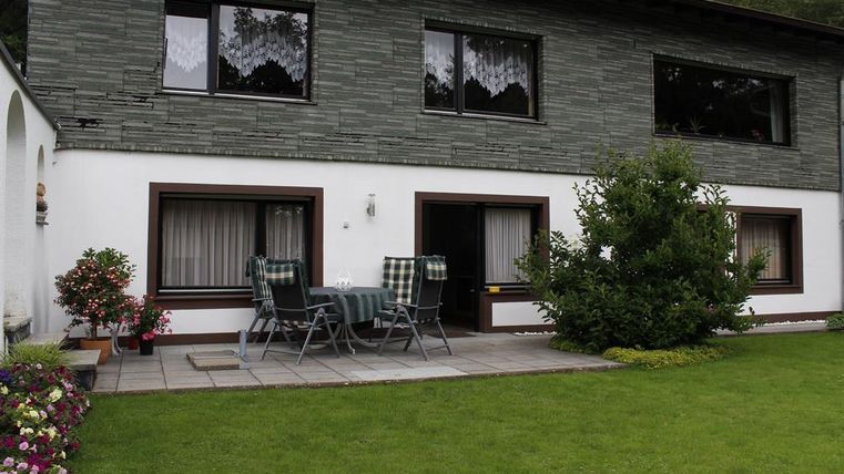 Een modern huis met twee verdiepingen en grote ramen. Buiten is er een terras met tuinmeubelen en een onderhouden gazon.