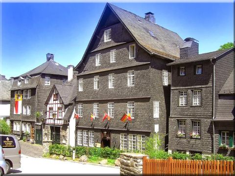 Eine malerische Sicht auf historische Fachwerkhäuser mit dunkelbraunen Fassaden. In der Straße wehen Fahnen und es ist ein klarer, blauer Himmel zu sehen.