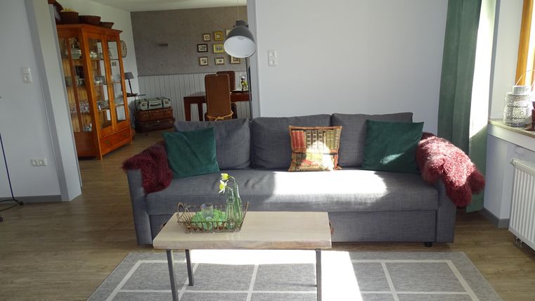 Een sfeervolle woonkamer met een grijze bank en een houten tafel. De ruimte is helder verlicht en heeft een uitnodigende sfeer.