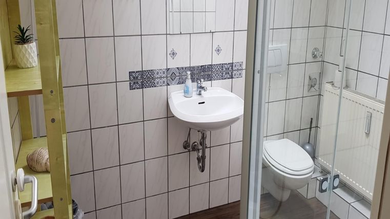 Een moderne badkamer met een wastafel, een douche en een toilet. De muren zijn voorzien van lichte tegels en decoratieve patronen.