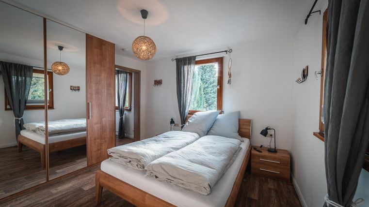 Een gezellige slaapkamer met een tweepersoonsbed en meubels van hout. Grote ramen zorgen voor veel daglicht en een ontspannen sfeer.
