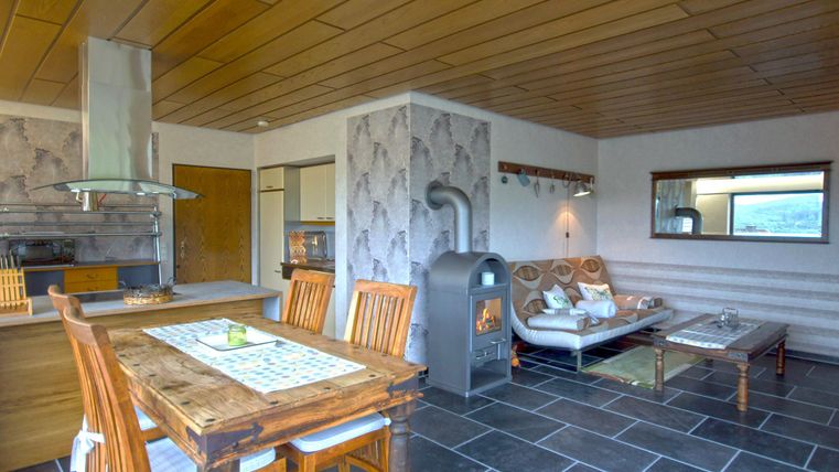 Ein modernes Wohnzimmer mit einem Esstisch aus Holz und einem gemütlichen Sofa. Der Raum hat große Fenster und einen Kamin, der eine warme Atmosphäre schafft.