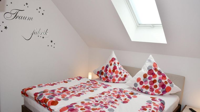 Een gezellige slaapkamer met een tweepersoonsbed en kleurrijke kussens. Aan de muur staat de tekst "Droomfabriek".