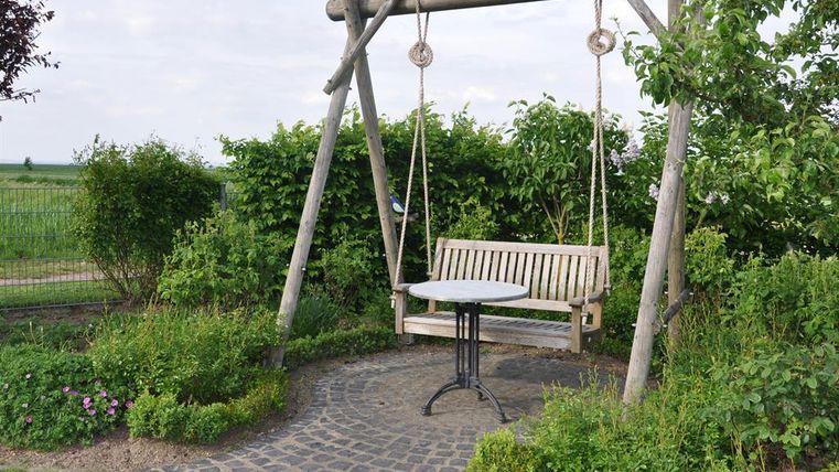 Eine gemütliche Holzschaukel steht in einem grünen Garten. Neben der Schaukel befindet sich ein runder Tisch.