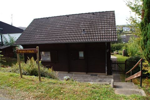 Een rustiek vakantiehuis met een bruine houtgevel. Het staat in een groene omgeving met een kleine tuin en een pad naar de voordeur.