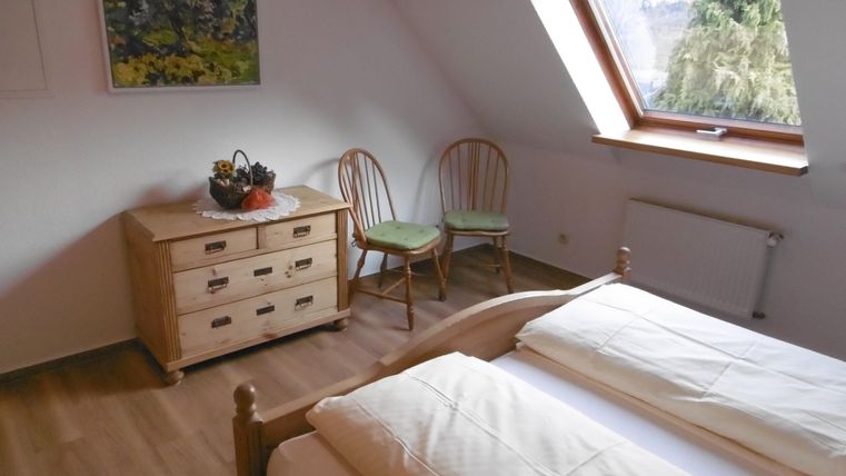 A simple room with two single beds and a window that lets in a lot of light. In the room, there is a wooden table and two chairs, as well as a dresser.