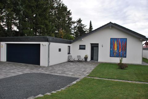 A modern house with a large garage door and colorful artwork on the wall. In the foreground, there is a well-maintained garden with a seating area.