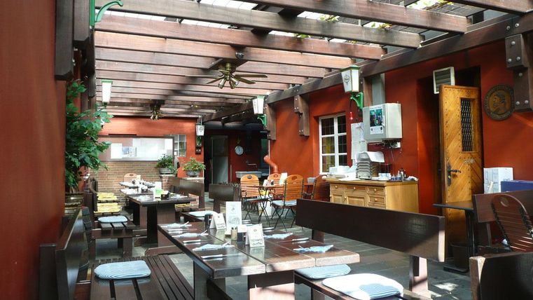 Een uitnodigende buitenruimte van een restaurant met houten meubels en begroeide muren. De zonneschijn zorgt voor een vriendelijke sfeer.