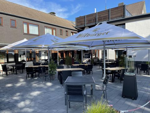 An inviting terrace with tables and chairs under large sun umbrellas. In the background, a building can be seen that creates a relaxed atmosphere.