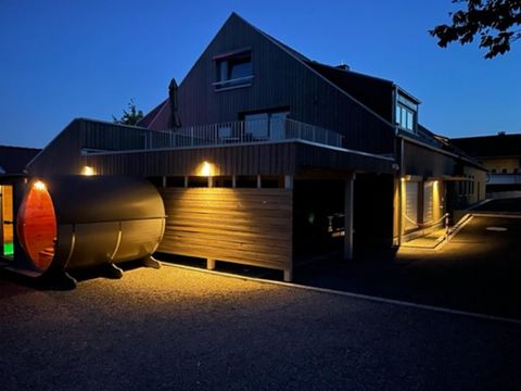 Een modern gebouw bij nacht, verlicht door warme lichten. Aan de linkerkant staat een kenmerkende sauna met een ronde vorm.