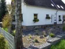 Een mooi huis met witte muren en een tuin van grind. Kleurrijke bloempotten sieren de ramen.