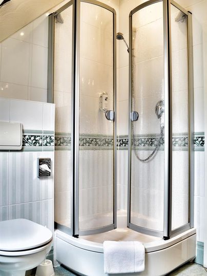 A modern bathroom with a three-sided shower and a toilet. The walls are brightly tiled and there is a towel rack.