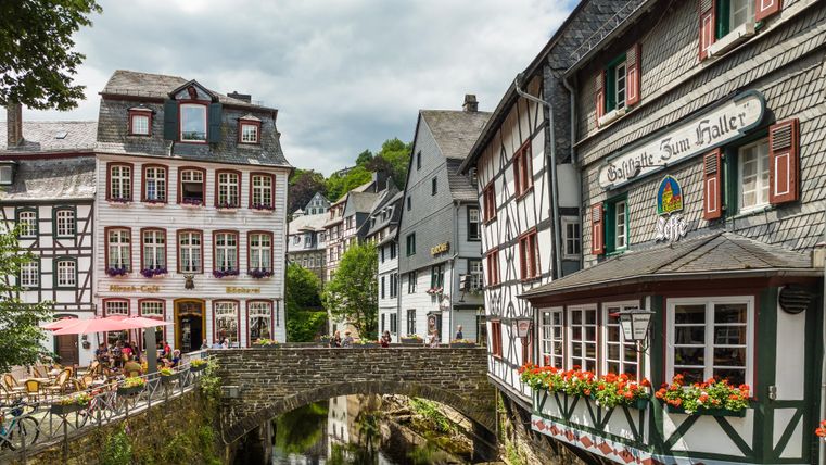 Eine malerische Stadtansicht mit historischen Fachwerkhäusern und einem kleinen Bach. Die Umgebung ist grün und einladend.