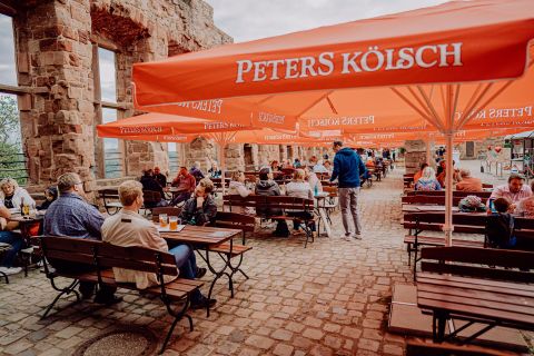 An inviting outdoor terrace with tables and chairs under orange umbrellas. Guests enjoy drinks in a rustic setting.