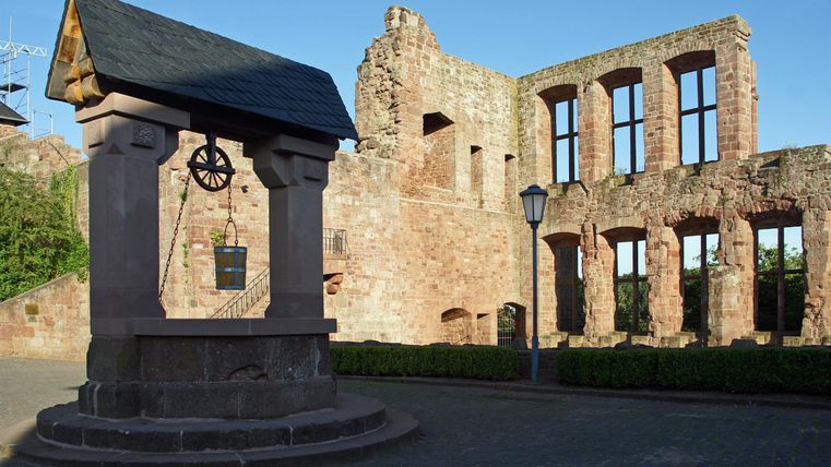 Een oude ruïne met grote ramen en een historische fontein op de voorgrond. De zon schijnt op de stenen muren en zorgt voor een schilderachtige sfeer.