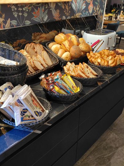 A selection of fresh bread and rolls in baskets. In the foreground, snacks and sweets are also visible.