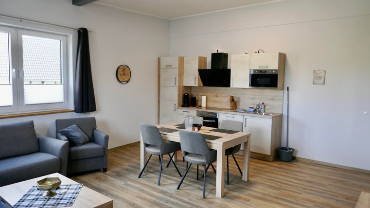 A modern living room with an open kitchen. There is a dining table with chairs and a cozy couch.