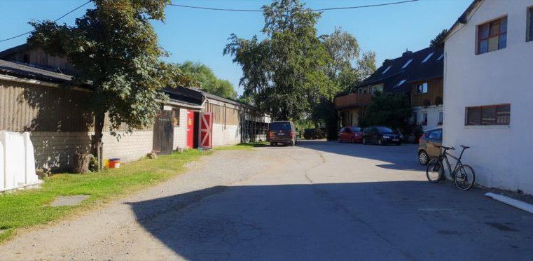 Eine ruhige Straße mit Garagen und Wohngebäuden. Bäume und ein Fahrrad sind sichtbar.
