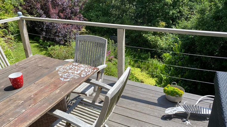 Een gezellige balken met een houten tafel en stoelen. Op de achtergrond zie je weelderig groen en een mooie plantenlandschap.
