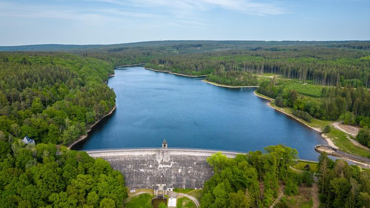 Ein ruhiger Stausee umgeben von grünen Wäldern. Die Landschaft ist idyllisch und lädt zur Erholung ein.