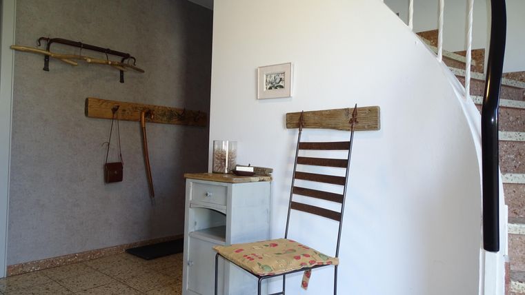 Een gezellige hal met een stoel en een kleine commode. Aan de muur hangen decoratieve voorwerpen en een kunstwerk.