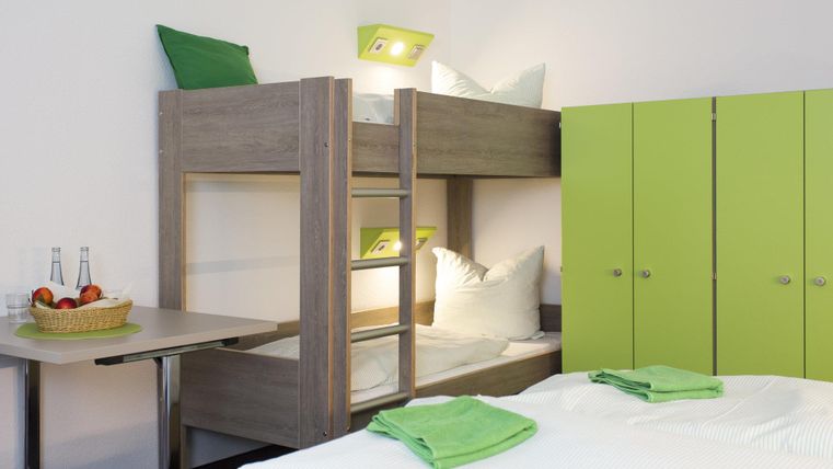 A functional room with a bunk bed and a double bed. The furniture is modern and in friendly colors.
