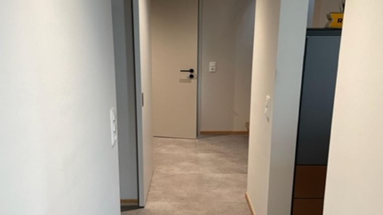 Een lange gang met lichte muren en tapijt. Aan het einde van de gang bevindt zich een gesloten deur.