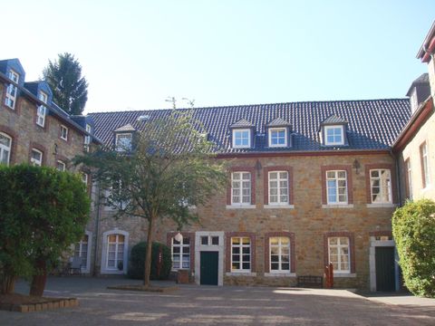 Ein historisches Gebäude mit einer warmen Steinfassade und vielen Fenstern. Im Innenhof stehen einige Bäume und es ist sonnig.