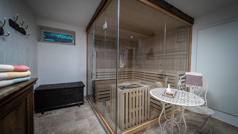 Een moderne saunaruimte met grote glaswanden. Naast de sauna staat een kleine tafel en een gezellige zitgelegenheid.
