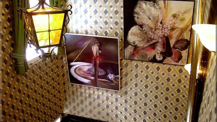Ein stilvoller Treppenaufgang mit einer dekorativen Lampe und kunstvollen Bildern an der Wand. Die Wände sind mit einem eleganten Muster versehen.