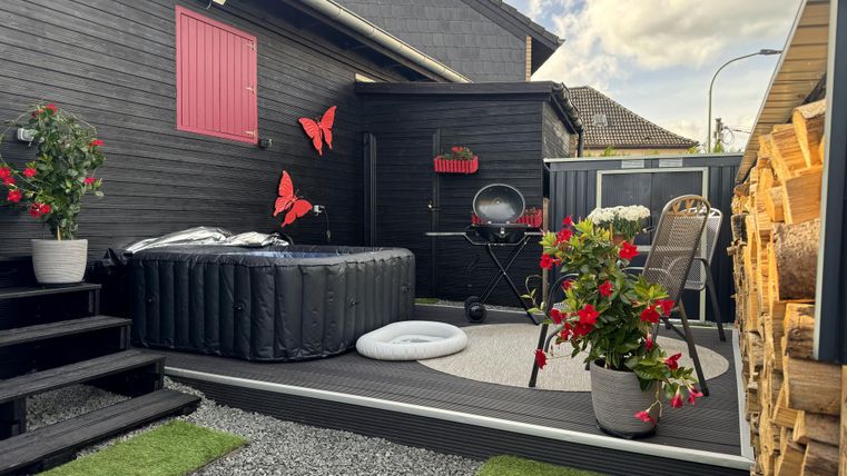 Een gezellige buitenruimte met een opblaasbare jacuzzi, planten en rode vlinders. Een uitnodigend terras met een barbecue en zitgelegenheid.