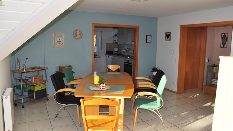 A bright dining area with a round table and colorful chairs. In the background, a modern kitchen is visible.