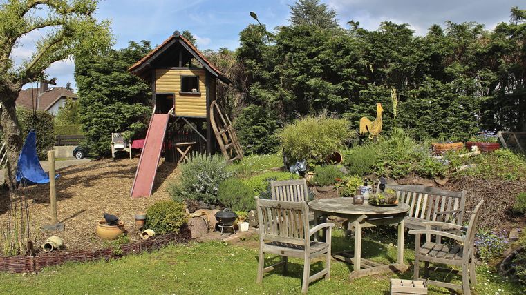 A beautiful garden with a playhouse and a slide. Comfortable furniture invites you to relax.
