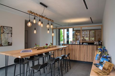 A modern foyer with a long wooden table and stylish chairs. Informational materials are on the wall and large windows provide plenty of natural light.