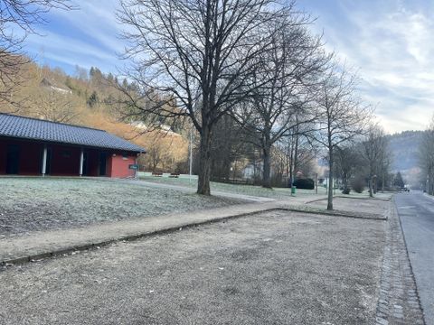 A quiet park with bare trees and frosty ground. In the background, buildings and gentle hills can be seen.