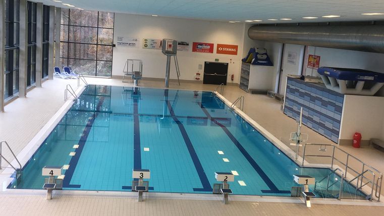 Ein modernes Schwimmbad mit klarem Wasser und Startblöcken. Viel Tageslicht fällt durch große Fenster in den Raum.