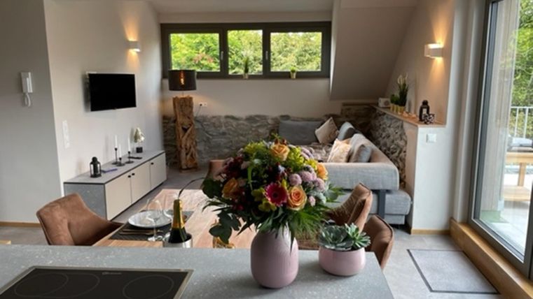 Een moderne woonkamer met een gezellige bank en grote ramen die veel licht binnenlaten. Een mooie bos bloemen in een vaas staat op de tafel.