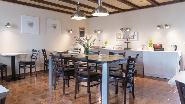 A cozy dining room with wooden tables and chairs. Pictures are hanging on the walls, and a plant is on the table.