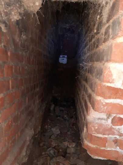 Een smalle, donker uitziende tunnel van bakstenen met stenen en puin op de bodem. Aan het einde van de tunnel is een zwak licht zichtbaar.