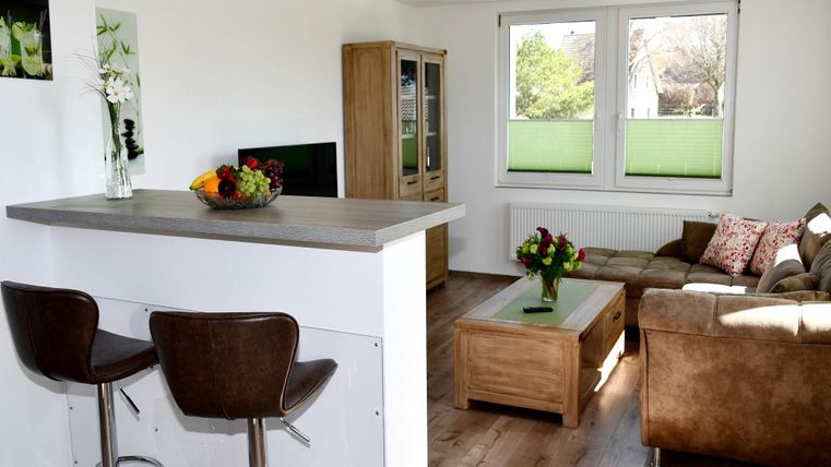 Een heldere en moderne woonkeuken met een gezellige bank en een salontafel. Op de achtergrond zie je grote ramen die veel daglicht binnenlaten.