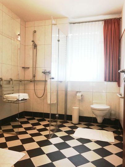 Een moderne badkamer met een zwart-witte tegelvloer. Het beschikt over een inloopdouche, handdoeken en een grote raampartij.