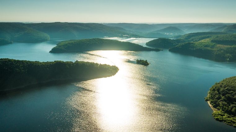 A picturesque lake with gentle hills and lush greenery. The sunlight gleams brilliantly on the surface of the water.