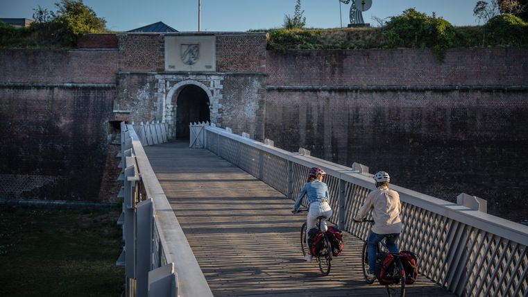 Zwei Radfahrer fahren auf einer Brücke aus Holz vor der Zitadelle Jülich