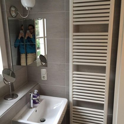 A modern bathroom with a sink and a towel radiator. A mirror and a lamp are also visible.